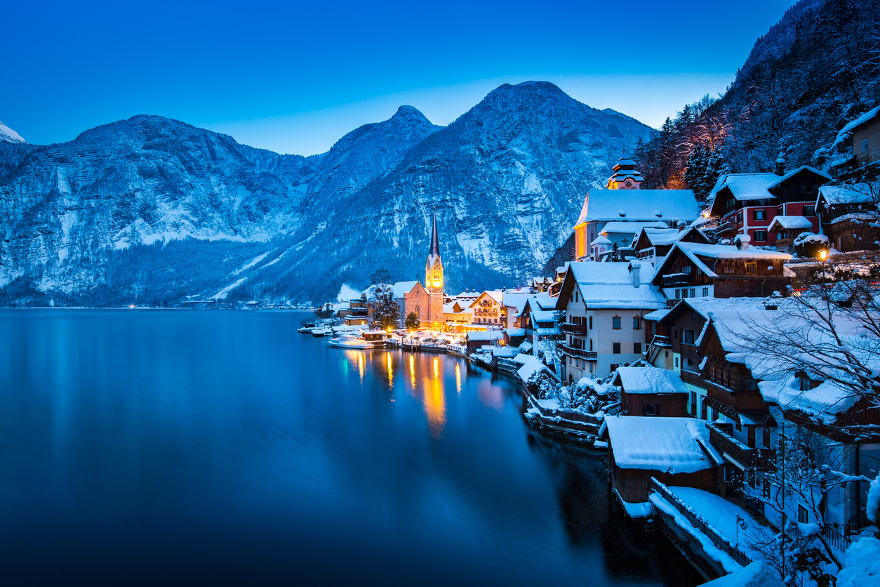 Classic postcard view of famous Hallstatt lakeside town in the Alps with beautiful Hallstattersee in mystical post sunset twilight during blue hour at dusk in winter, Salzkammergut, Austria