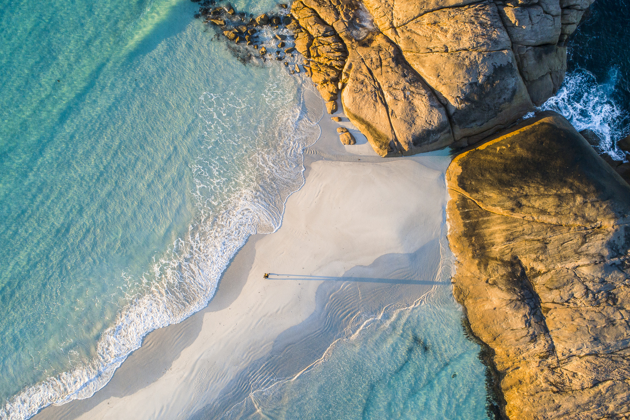 Coastline aerial photograph of aquamarine ocean and man walking along white sandbar beach