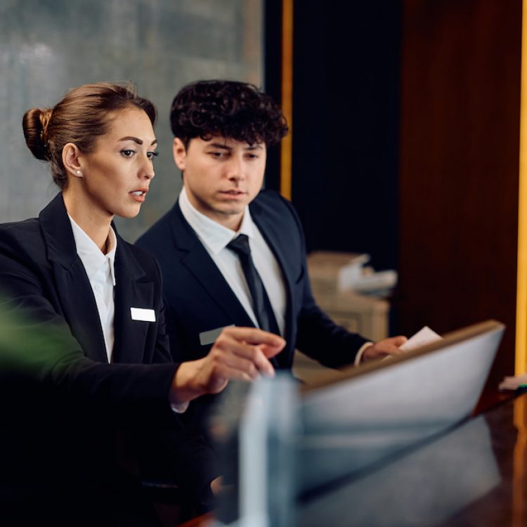 Female concierge assisting receptionist while using desktop PC in a hotel.