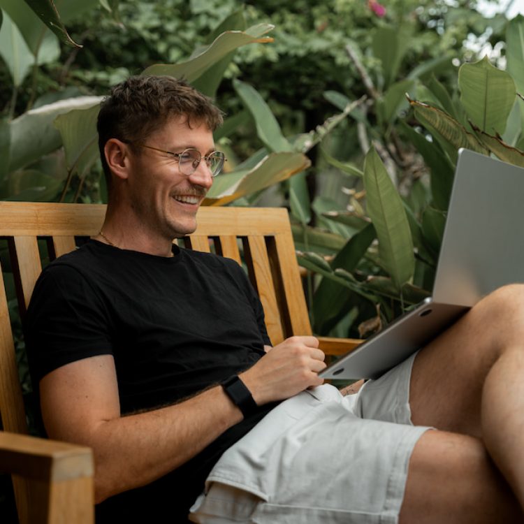 Man speaks on laptop in tropical garden
